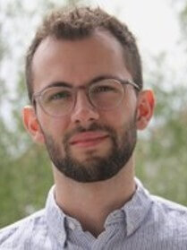 David Moser mit Brille und Bart, heller Hintergrund, ernster Blick.